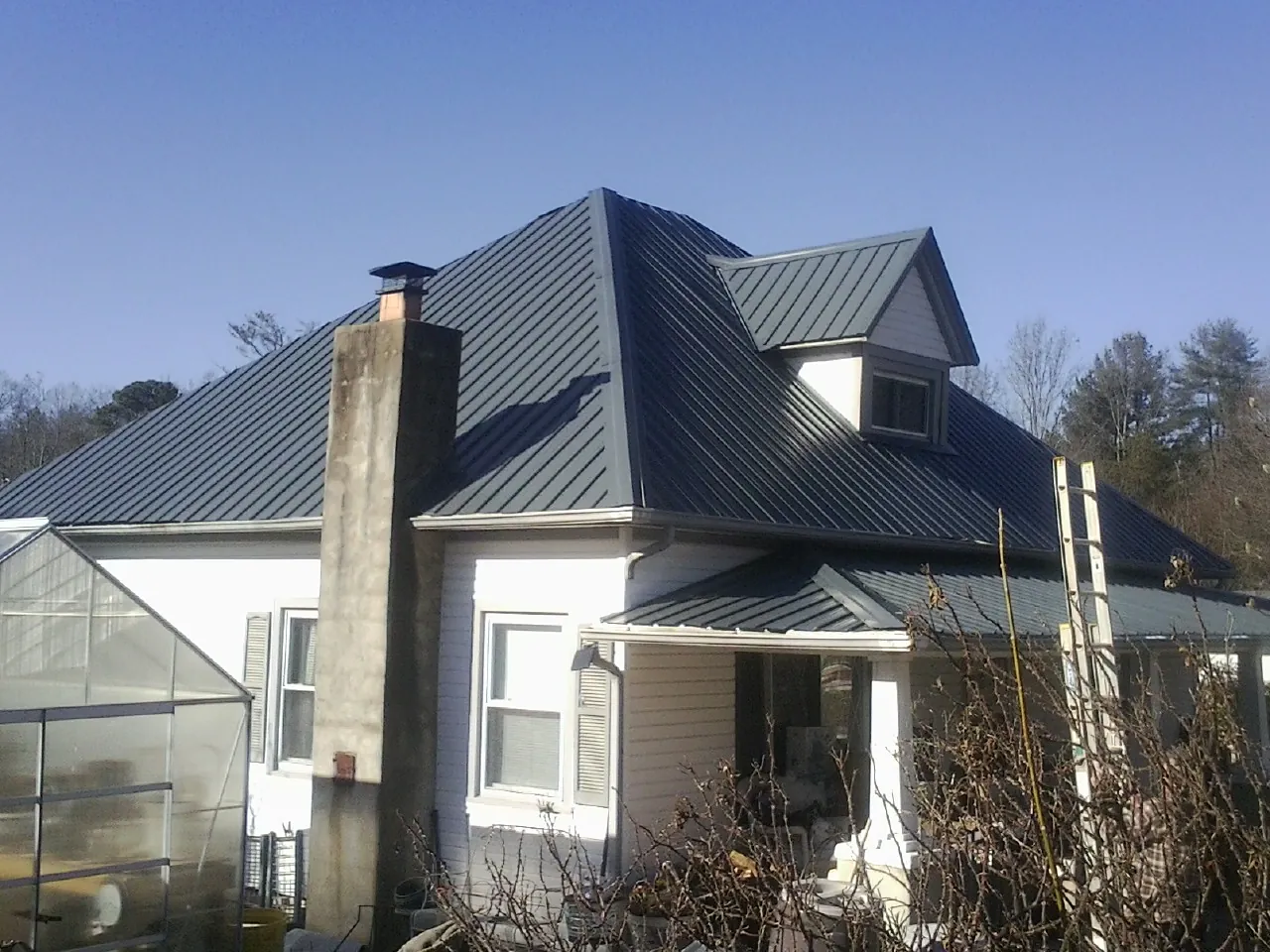 Dark blue standing seam metal roof on a white farmhouse with dormer — Slate & Tile Roof Repair by Roofing Brothers in Sweet