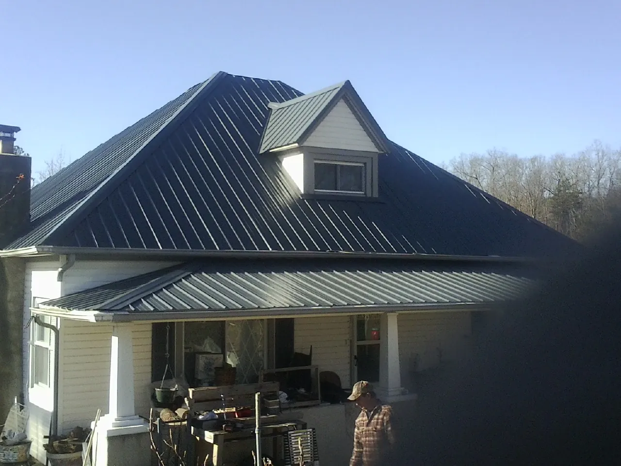 Dark blue standing seam metal roof with a dormer above a front porch in Sweet
