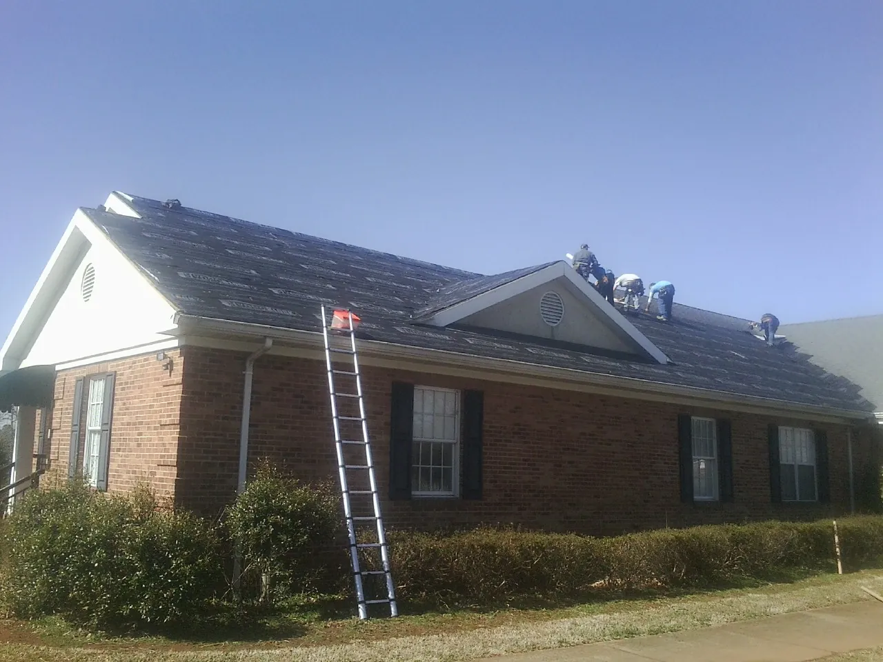 Crew tearing shingles off a brick ranch roof with a ladder set — Emergency Roof Repair work by our crew in Sweet
