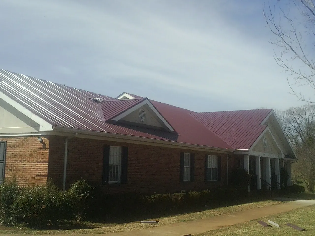 Red metal roof with gabled entries on a long brick building, from a Hail Damage Roof Repair job in Sweet