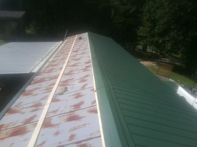Old rusted panels beside newly installed green metal roofing — Wind Damage Roof Repair by Roofing Brothers in Sweet