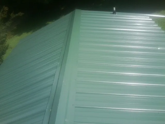 New green metal panels meeting at the ridge of a roof — Flat Roof Repair work by our crew in Sweet