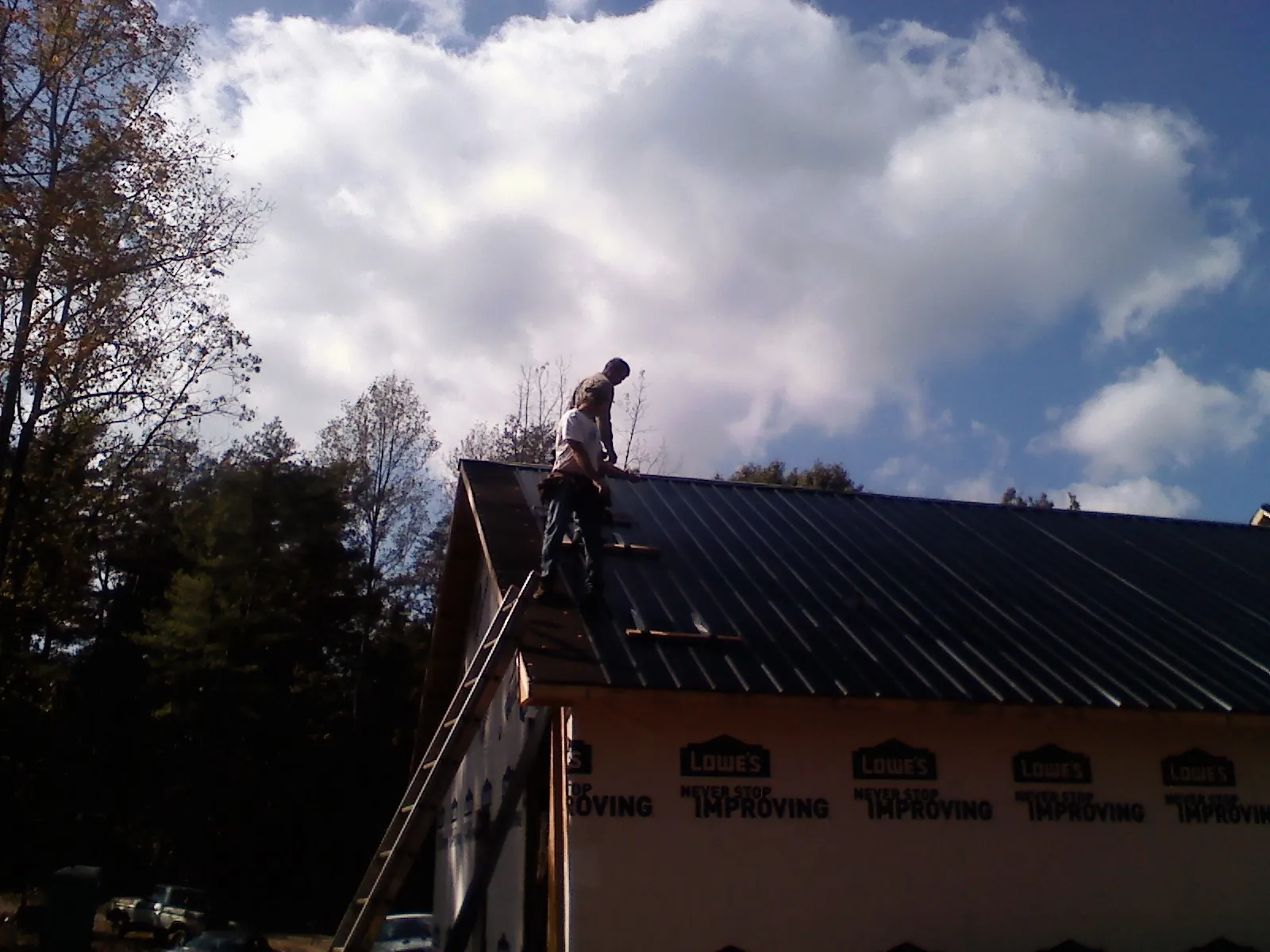Roofer fastening dark metal panels high against a cloudy sky, from a Roof Inspection job in Sweet