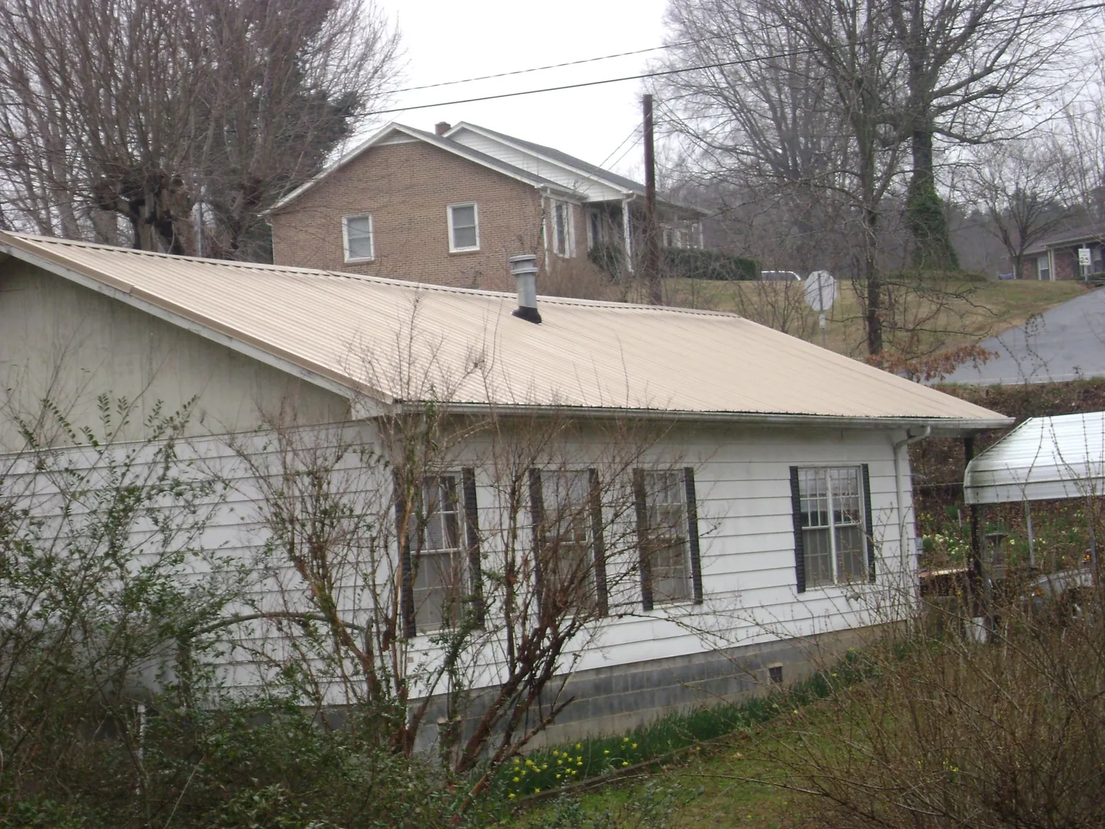 Tan metal roof on a white sided house set into a hillside — Commercial Roofing by Roofing Brothers in Sweet