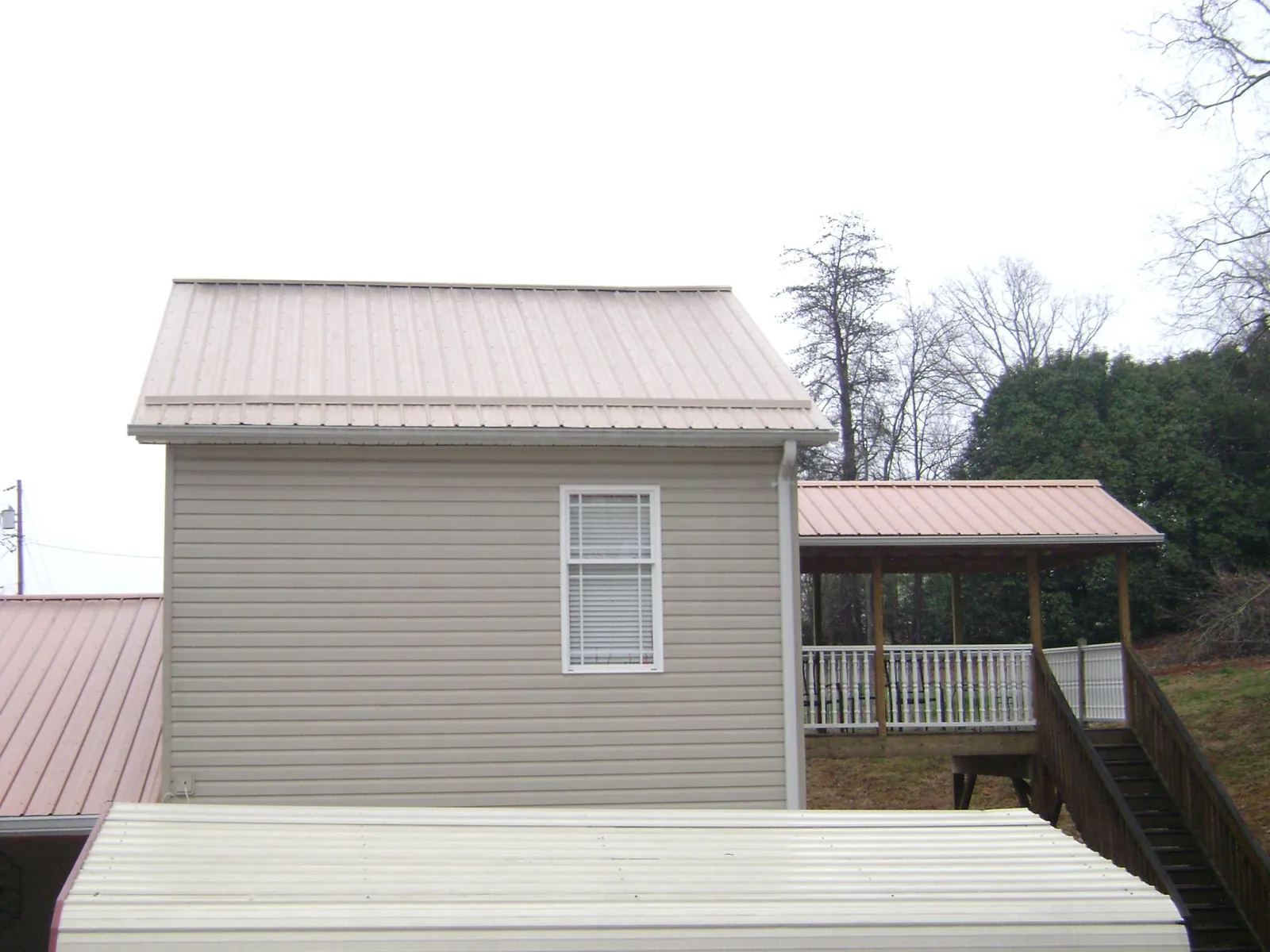 Tan metal roofs on a two story addition and attached porch, from a Roof Replacement job in Sweet